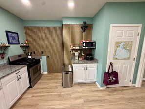 A compact kitchen with a stove, microwave, and coffee maker, a striped wall, and a door with a map. - Your Lake Escape Starts at Balti Bay Lodge New Baltimore 3 bedroom, Boat Parking (New Baltimore)