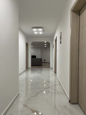 Un couloir au sol en marbre mène à un salon équipé d’un canapé et d’un téléviseur.