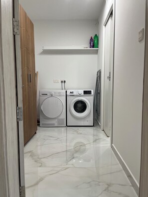 A laundry room with two washing machines, a wooden door, and a white tiled floor. - WiFi - 2min walk to sea - Modern 2 BR Corner Ground Floor with large terrace (San Pawl il-Baħar)