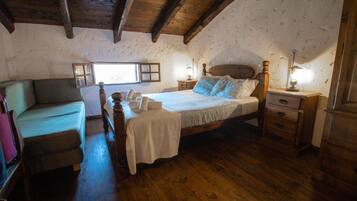A bedroom with a wooden bed, a bedside table, a nightstand, a chair, and a window.