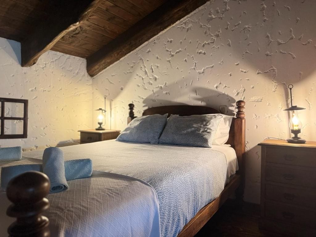 A bedroom with a wooden ceiling, a bed with a white and blue bedspread, two bedside lamps, and a wooden nightstand.