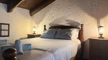 A bedroom with a wooden ceiling, a bed with a white and blue bedspread, two bedside lamps, and a wooden nightstand.