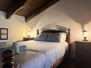 Ein Schlafzimmer mit Holzboden, einem Bett mit weißblauer Bettdecke, zwei Nachttischlampen und einem Nachttisch aus Holz.
