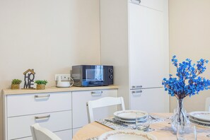 Una cocina moderna con armarios blancos, un microondas y una mesa de comedor para dos personas, con platos y vasos.
