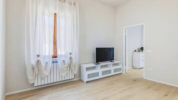 Una habitación con un televisor sobre un soporte blanco, un armario blanco y una puerta.