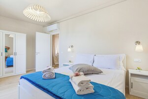 Una camera d'albergo con un letto, un armadio, un comodino e una lampada a sospensione.