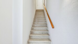 Uma escadaria com corrimão de madeira que leva a uma porta branca no topo.