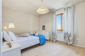 A bedroom with a bed, bedside lamps, a dresser, a window with curtains, and a radiator. - Clara's Olivi (Lavaiano)