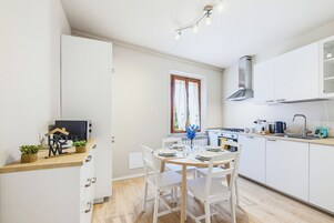 Una cocina moderna con armarios blancos, una mesa de comedor para cuatro personas y una ventana con cortinas.