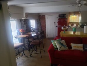 Un coin repas avec une table et des chaises, une cuisine équipée d’un four à micro-ondes et un canapé rouge agrémenté de coussins.