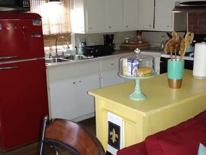 Une cuisine avec un réfrigérateur rouge, un îlot de cuisine jaune et une chaise en bois.