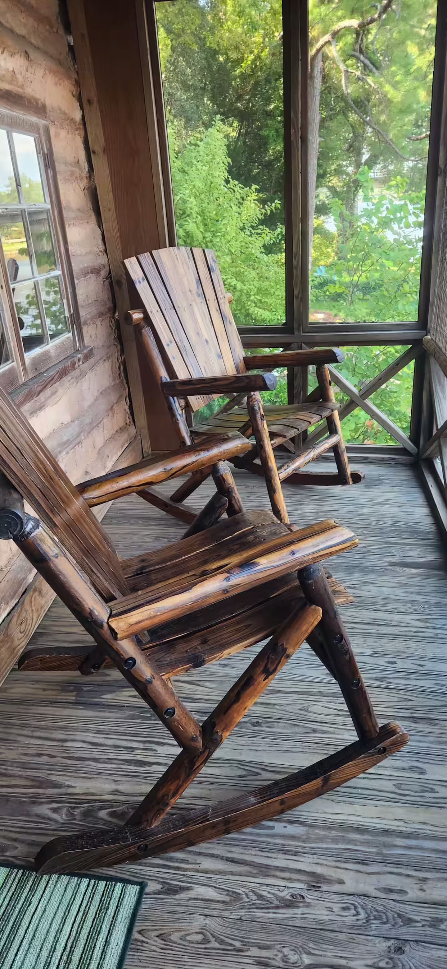 A rustic wooden rocking chair on a porch with a view of greenery.