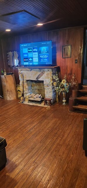 A room with a stone fireplace, wooden flooring, a flat-screen TV mounted above it, and a wooden wall.