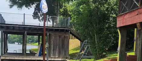 Un'area verde con un molo di legno che si estende in un corpo d'acqua, una recinzione metallica e un edificio con tetto rosso.