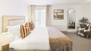 A hotel room with a bed, bedside lamp, a mirror, a chair, and a plant. - Large, Bright Westminster Apartment with Balcony (Greater London)