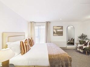 A hotel room with a bed, bedside lamp, a mirror, a chair, and a plant. - Large, Bright Westminster Apartment with Balcony (Greater London)