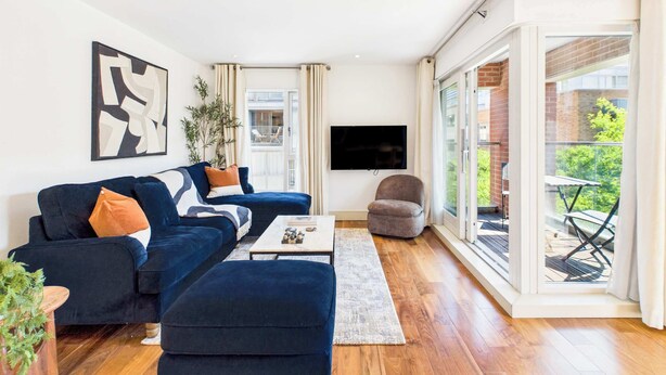 A modern living room with a sofa, ottoman, and a flat-screen TV. - Large, Bright Westminster Apartment with Balcony (Greater London)