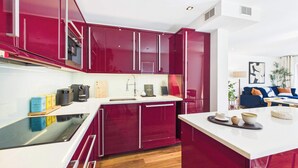 A modern kitchen with red cabinets, a white countertop, and a wooden floor. - Large, Bright Westminster Apartment with Balcony (Greater London)