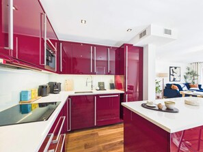 A modern kitchen with red cabinets, a white countertop, and a wooden floor. - Large, Bright Westminster Apartment with Balcony (Greater London)