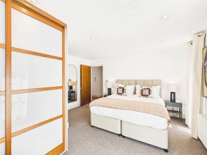 Una habitación de hotel con una cama grande, un armario correderas de madera, una mesita de noche con lámpara y un espejo en la pared.
