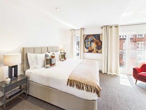 Ett hotellrum med en stor säng, sängbord, en röd stol, ett fönster med utsikt över byggnader och en tavla på väggen.