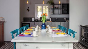 Een eethoek met een tafel voor vier personen, stoelen, een vaas met bloemen en een keuken op de achtergrond.