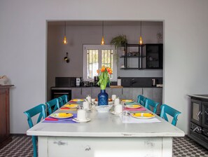 A dining area with a table set for four, chairs, a vase with flowers, and a kitchen in the background. - A renovated farmhouse in the heart of the Langhe, 7 km from Alba. (Piemonte)