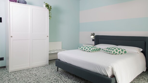 Een slaapkamer met een bed, een kledingkast, een nachtkastje en een hanglamp.