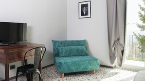 A room with a wooden desk, a teal chair, a framed picture on the wall, and a window with a curtain.