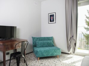 A room with a wooden desk, a teal chair, a framed picture on the wall, and a window with a curtain. - A renovated farmhouse in the heart of the Langhe, 7 km from Alba. (Piemonte)