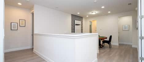 Un amplio espacio de estar con una isla central, una mesa de comedor con sillas y una puerta que da a otra habitación.