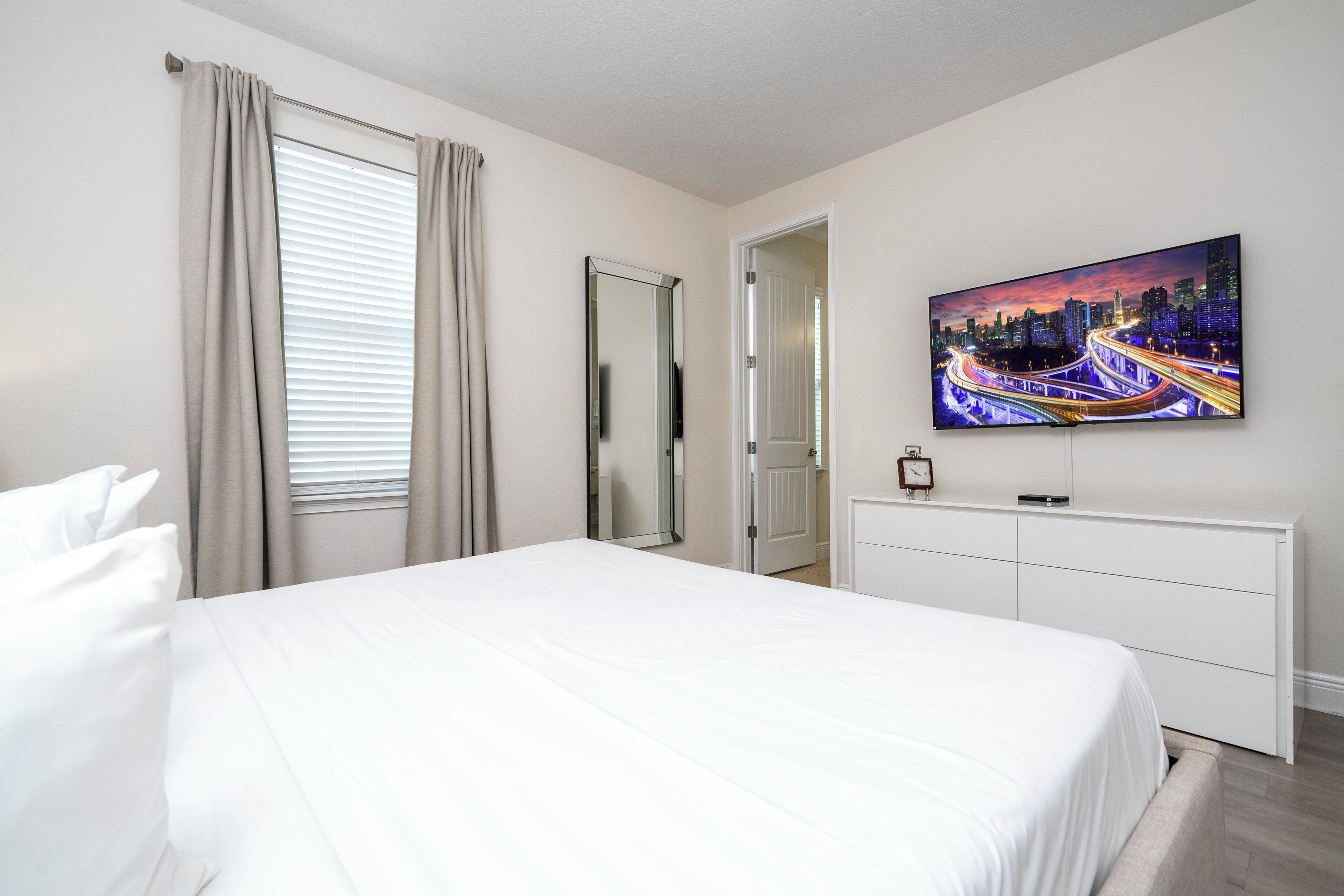 Habitación de hotel con cama, televisor en la pared, puerta y ventana con cortinas.