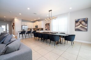 Una cocina moderna con armarios blancos, una isla central y un comedor con una mesa larga y sillas.