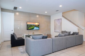 Ein modernes Wohnzimmer mit einem grauen Ecksofa, einem flachbildfernseher an der Wand, einer Treppe und einer weißen Tür.