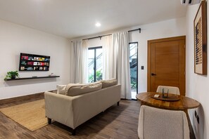 Un salon moderne comprenant un canapé, un téléviseur fixé au mur, une table à manger avec des chaises et une porte-fenêtre coulissante donnant sur un balcon.