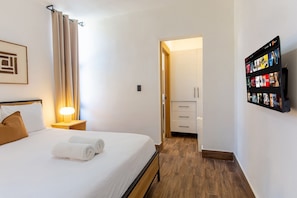 A hotel room with a bed, a bedside lamp, a wall-mounted TV, and a door leading to a hallway. - First-floor apartment 7 minutes from the beach (Punta Cana)
