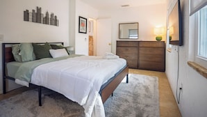 A bedroom with a bed, a ceiling fan, a dresser, a mirror, and a wall-mounted TV. - Gulfport Getaway - Beach, Downtown, Shops nearby (South Pasadena)