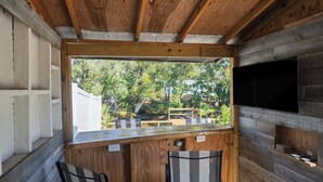 A small wooden room with a window, two chairs, a flat-screen TV, and a shelf with items. - Gulfport Getaway - Beach, Downtown, Shops nearby (South Pasadena)