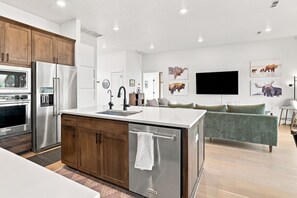 A modern kitchen with a central island, stainless steel appliances, and a dining area with a green sofa. - 4 Peaks Post | 25min to Grand Targhee, Sleeps 18, Hot Tub, Views! (Tetonia)