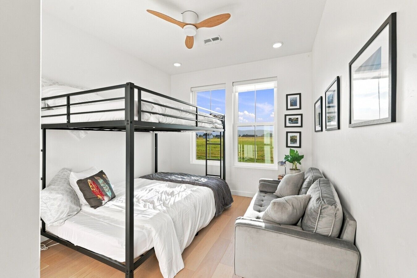 A bunk bed room with a ceiling fan, a sofa, and framed pictures on the wall.
