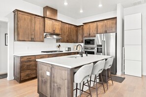 Eine moderne Küche mit Holzschränken, Edelstahlgeräten und einer zentralen Kochinsel mit Barhocker.