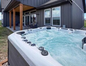 A hot tub with a wooden deck and chairs, set against a house with large windows. - 4 Peaks Post | 25min to Grand Targhee, Sleeps 18, Hot Tub, Views! (Tetonia)