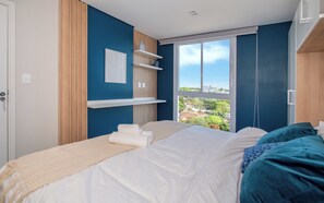 A bedroom with a bed, a window with a city view, and built-in shelves. - Corporate Stays First Living - 806 (Asunción)