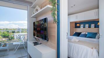 A modern bedroom with a bed, a TV mounted on the wall, and a balcony with a chair.