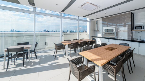 A modern office space with a large table and chairs, a kitchen area, and a view of a city skyline through large windows. - Corporate Stays First Living - 806 (Asunción)