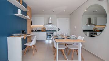 Una cocina moderna con armarios blancos, una isla central y un área de comedor con un espejo redondo.
