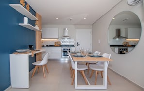 Una cocina moderna con armarios blancos, una isla central y un área de comedor con un espejo redondo.