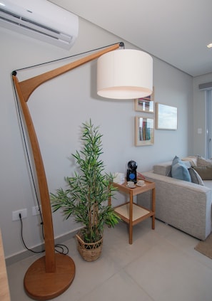 A modern living room with a floor lamp, a potted plant, a coffee table with a kettle and cups, and a sofa with cushions. - Corporate Stays First Living - 806 (Asunción)