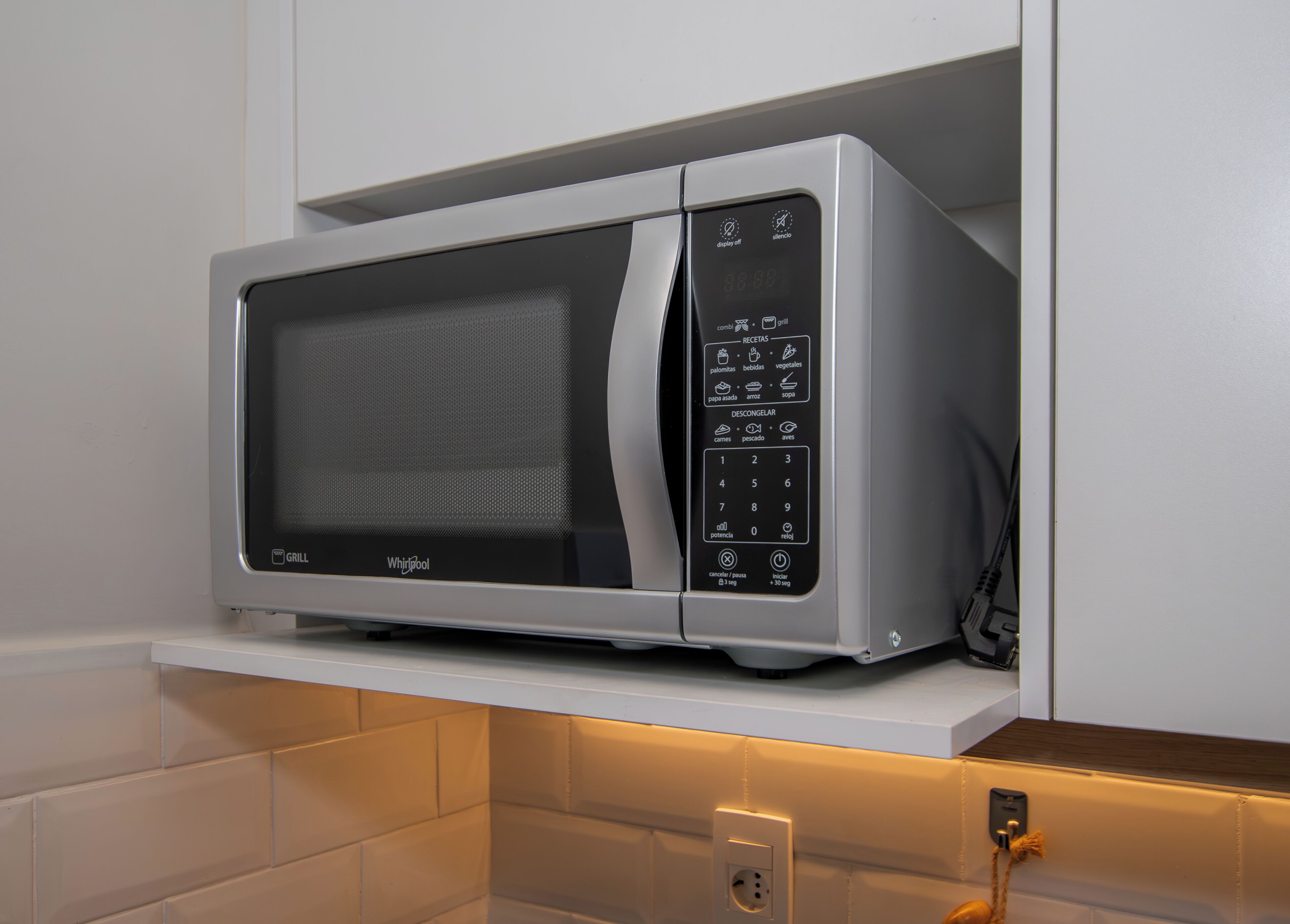 En mikrovågsugn från Whirlpool med en digital display och en kontrollpanel, placerad på en vit hylla.