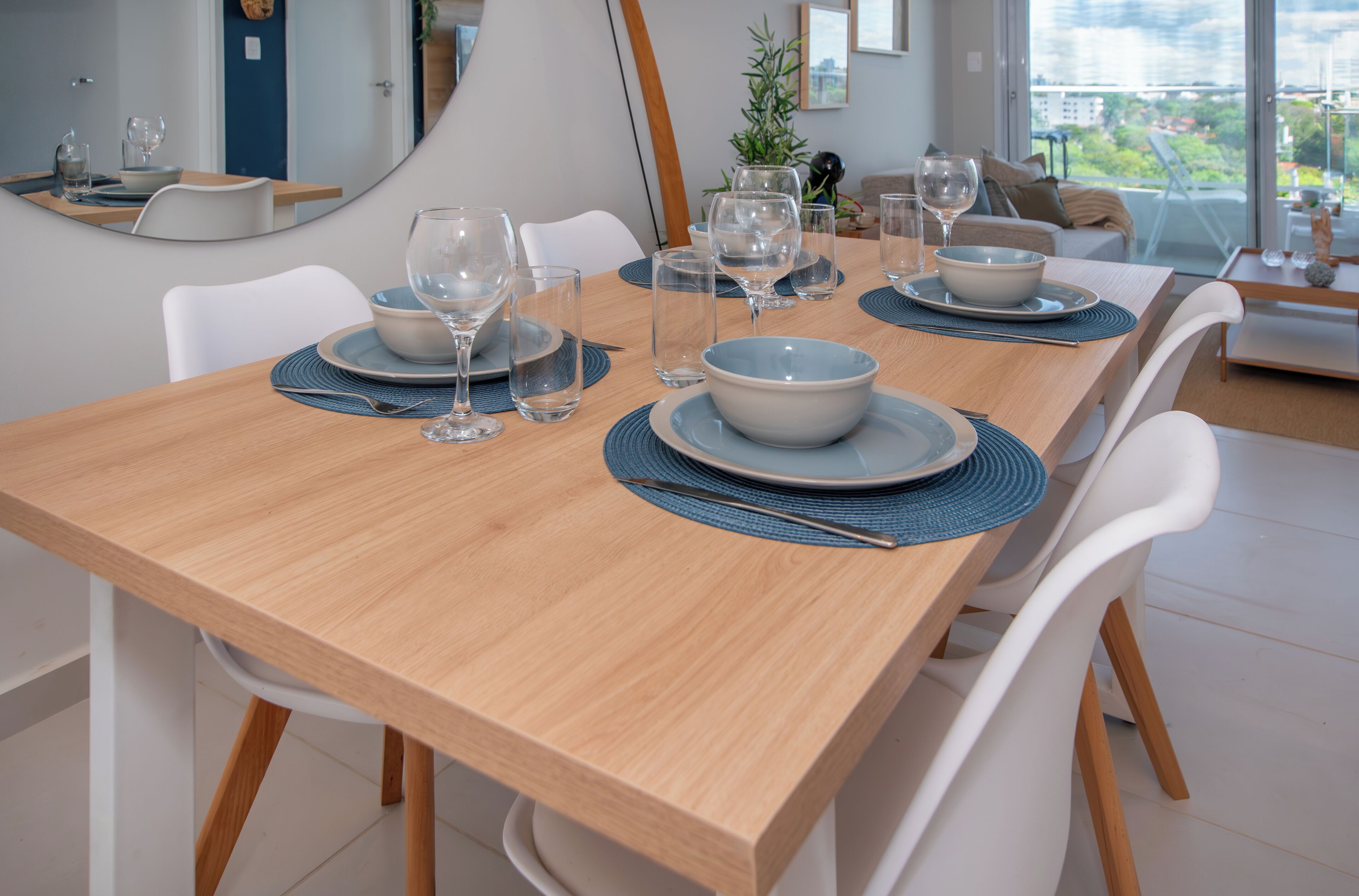 A dining table set with plates, bowls, and wine glasses, surrounded by white chairs.